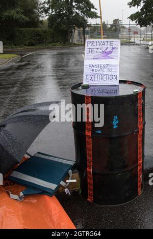 Farnborough, Royaume-Uni. 2 octobre 2021. Un activiste du climat de la rébellion de l'extinction est enfermé à un baril de carburant afin de bloquer une entrée à l'aéroport de Farnborough. Des activistes ont bloqué trois entrées de l'aéroport privé pour mettre en évidence les niveaux élevés de dioxyde de carbone produits par les passagers très riches utilisant des jets privés et le « lavage vert » par l'aéroport en annonçant un passage au carburant aviation durable (SAF). Crédit : Mark Kerrison/Alamy Live News Banque D'Images