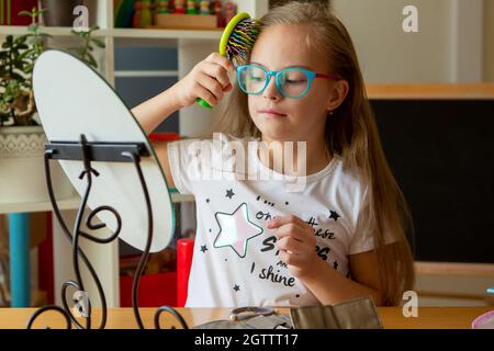 Belle fille avec le syndrome de Down peignant ses cheveux devant un miroir à la maison Banque D'Images