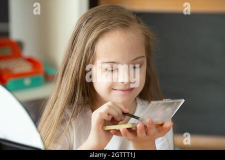 Belle fille avec le syndrome de Down peignant ses cheveux devant un miroir à la maison Banque D'Images