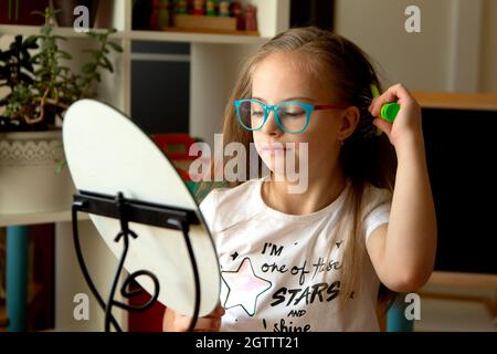 Belle fille avec le syndrome de Down peignant ses cheveux devant un miroir à la maison Banque D'Images