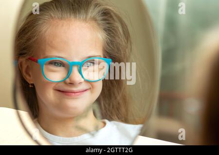 Belle fille avec le syndrome de Down peignant ses cheveux devant un miroir à la maison Banque D'Images