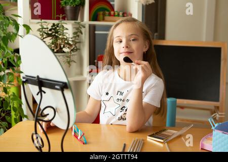 Belle fille avec le syndrome de Down peignant ses cheveux devant un miroir à la maison Banque D'Images