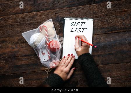 Liste de cadeaux de Noël, garde des cadeaux de Noël. Mains de femmes avec bloc-notes ouvert et texte liste de cadeaux sur fond de bois Banque D'Images