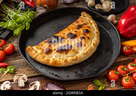 Pizza calzone sur une assiette noire avec des légumes Banque D'Images