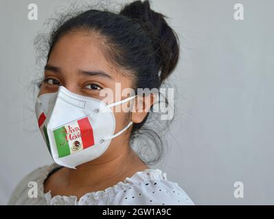 Une jolie fille mexicaine, patriotique à yeux bruns, porte un masque de style KN95 avec le drapeau mexicain pendant la pandémie du coronavirus et regarde le spectateur. Banque D'Images