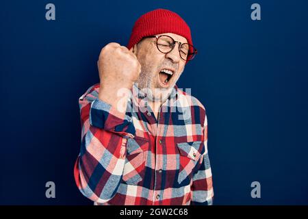 Beau homme mûr portant le look hippster avec la casquette de laine en colère et fou levant poing frustré et furieux tout en criant avec colère. Rage et agressivité Banque D'Images