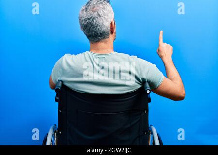 Beau homme d'âge moyen aux cheveux gris assis sur un fauteuil roulant en se posant vers l'arrière en pointant vers l'avant avec le doigt de la main Banque D'Images