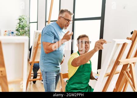 Groupe d'étudiants en peinture d'âge moyen qui dessinant au studio d'art. Professeur avec l'expression sérieuse regardant le dessin étudiant. Banque D'Images