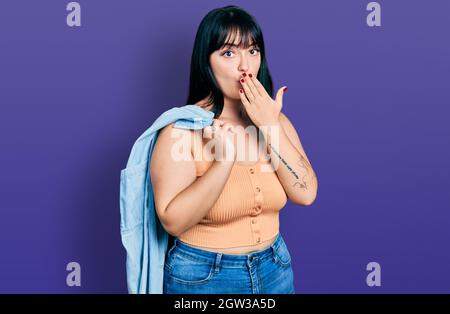 Jeune femme hispanique de taille plus portant une veste en denim couvrant la bouche avec la main, choquée et peur de l'erreur. Expression surprise Banque D'Images