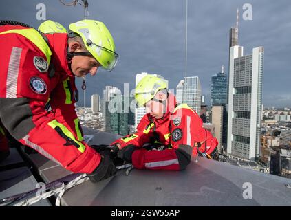 29 septembre 2021, Hessen, Francfort-sur-le-main : le secouriste de hauteur jusqu'à Fleckenstein (l) sécurise un camarade qui descend soigneusement au-dessus du bord de la tour 'Winx' de 110 mètres de haut pour descendre en rappel vers une gondole de nettoyage de fenêtre dans le cadre d'un scénario de formation. La moindre erreur peut être la chute des hommes de l'équipe de sauvetage en hauteur lors de leurs missions sur les gratte-ciels de la métropole bancaire. (À dpa « High up - height resevers in action in Extreme situations ») photo : Boris Roessler/dpa Banque D'Images