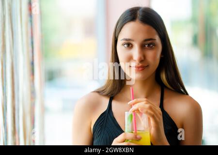 Une jeune femme souriant et buvant une boisson devant la fenêtre. Photo de haute qualité Banque D'Images