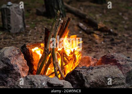 Camping feu de camp. Des branches brûlantes dans un foyer entouré de pierres. Crépuscule. Vue latérale. Mise au point sélective. Banque D'Images