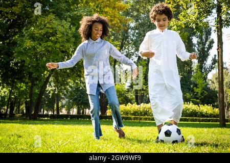 image cinématographique d'une famille des émirats passant du temps dans le parc. Frère et sœur jouant au football dans l'herbe Banque D'Images