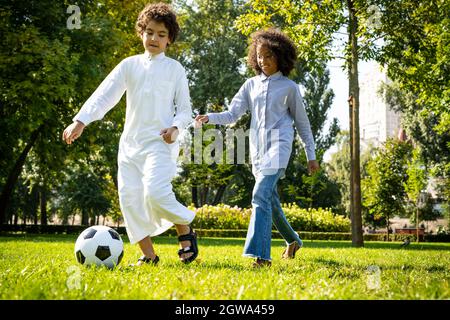 image cinématographique d'une famille des émirats passant du temps dans le parc. Frère et sœur jouant au football dans l'herbe Banque D'Images