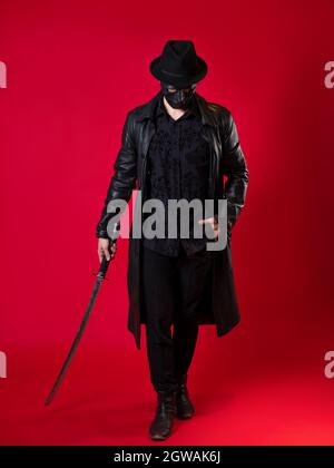 Un mystérieux assassin ninja dans un style noir. Un homme en cuir noir avec un manteau et un chapeau, couvre son visage avec un masque et utilise un katana. Photo Banque D'Images