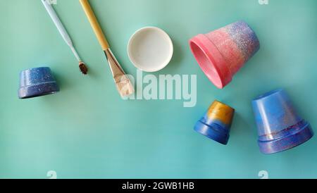 Pose à plat de pots en terre cuite colorés peints, pinceau, brosse à dents et un bac à peinture avec espace de copie dans le coin inférieur gauche. Banque D'Images