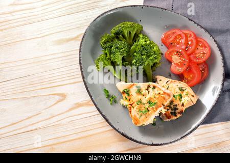 Tranches de thon avec brocoli et tomates sur une assiette grise et une table en bois clair, repas sain pour l'amincissement avec le régime cétogène ou bas carb, espace de copie Banque D'Images