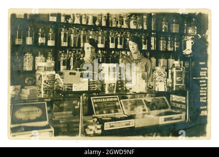 Carte postale originale et rare des années 1920 de l'intérieur typique, traditionnel à l'ancienne, boutique de bonbons, avec des propriétaires ou assistants féminins heureux, debout souriant derrière le comptoir, la célèbre marque Barker et Dobson confiseurs sur des pots en verre. Boutique victorienne, intérieur de boutique de bonbons. Par W Williams, Caernarvon, pays de Galles, Royaume-Uni vers 1927 Banque D'Images