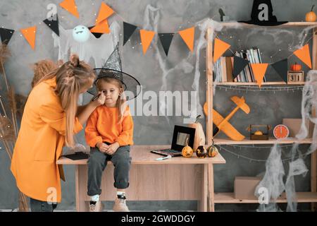 Femme et enfant se prépare pour les vacances d'Halloween. Maman applique le maquillage à l'enfant sous la forme d'un lion à la maison dans la chambre. Sorcière Banque D'Images