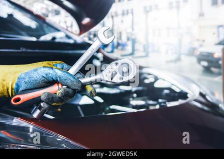 Mécanicien main tenant une clé pour la réparation de voiture dans le garage de réparation, concept de service d'entretien de voiture. Banque D'Images