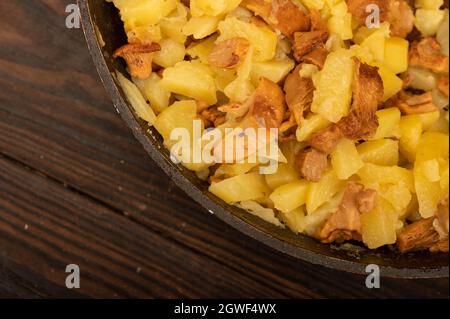 Pommes de terre frites dans une poêle avec champignons sur une table en bois. Un plat traditionnel de village Banque D'Images