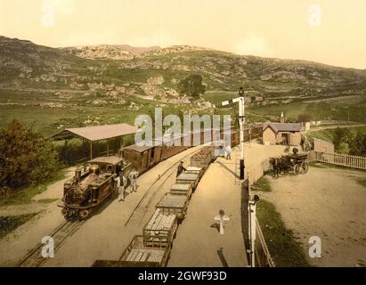 Photo couleur vintage vers 1890 d'une locomotive à vapeur à voie étroite Double Fairlie de la Ffestinog Railway Company avec des wagons d'ardoise transportant de l'ardoise des carrières locales et des voitures de passagers à la gare de Tan-y-Bwlch entre Blaenau Ffestinog et Porthmadog Banque D'Images