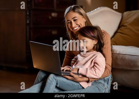 Heureux rire une mère célibataire et petite petite petite fille d'âge préscolaire mignon en utilisant un ordinateur portable, faisant appel vidéo, ayant amusement, babysitter enseignement petite fille utilisation comput Banque D'Images