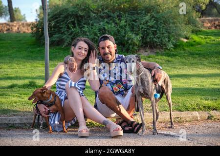 Jeune couple tatoué qui s'embrasse et s'assoit avec leurs chiens regardant l'appareil photo. Banque D'Images