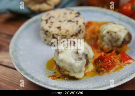 Gros plan de la plaque bleue sur une table en bois avec des boulettes de viande hachées maison grainées au fromage mozzarella dans une sauce tomate fraîche avec du riz Banque D'Images