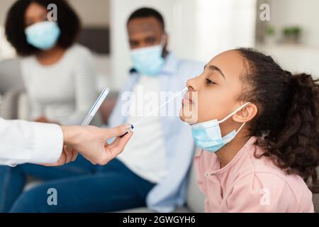 Test PCR du coronavirus nasal. Médecin utilisant un coton-tige pour prélever un échantillon de virus covid d'une jeune fille noire potentiellement infectée à la maison. Disea virale Banque D'Images