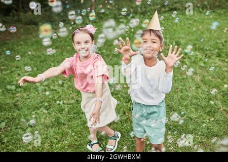 Portrait complet de deux jolies filles jouant avec des bulles tout en appréciant la fête d'anniversaire en plein air en été Banque D'Images