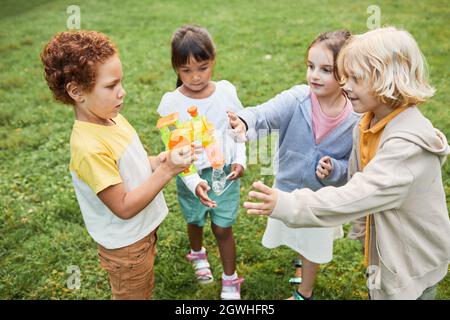 Portrait d'un groupe diversifié d'enfants jouant ensemble avec un jouet à bulles dans le parc Banque D'Images