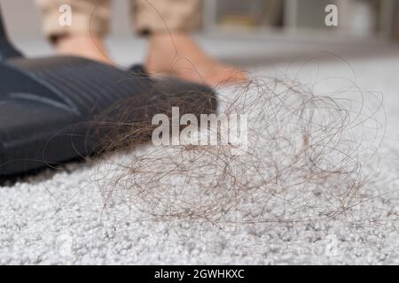 Une mèche de cheveux longs sur la moquette et un gros plan sur un aspirateur. Banque D'Images