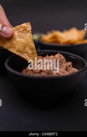 Trempant à la main la pastille de tortilla dans un bol de haricots réfrits Banque D'Images