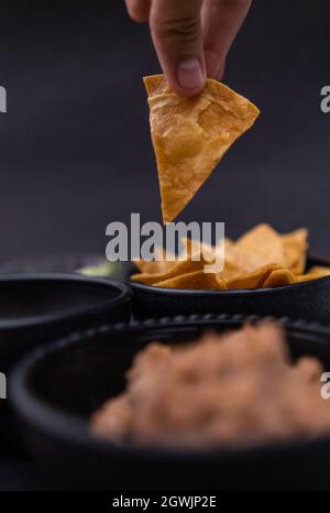 Cueillette à la main de la pastille de tortilla dans un bol à fond noir Banque D'Images