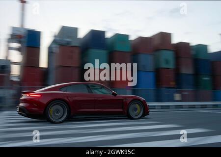 Antalya, Turquie 1er octobre 2021: Une cerise métallique, modèle électrique, Porsche Taycan Turbo S devant la zone des conteneurs sur un port commercial. Banque D'Images