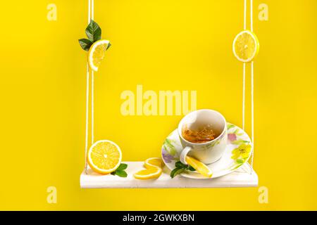 Tasse de thé assis sur une balançoire avec beaucoup de citron frais coupé autour et beau fond jaune vif Banque D'Images