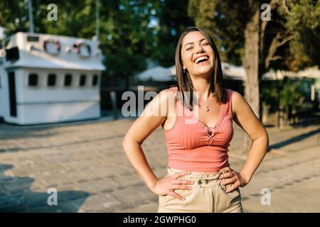 Une femme joyeuse et tendance souriante à l'extérieur - une jeune femme heureuse debout avec des bras à la taille dans la rue - Happiness et concept de jeunesse Banque D'Images