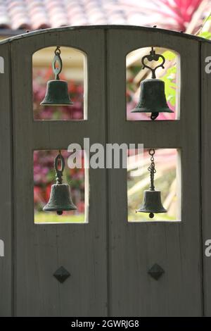 Belle porte en bois de style espagnol avec quatre cloches en métal vintage suspendues. Banque D'Images