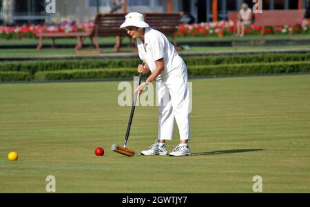 Une femme plus âgée en blanc joue du croquet à l'aide d'un maillet traditionnel pour frapper une balle rouge à Rotorua, en Nouvelle-Zélande. Banque D'Images