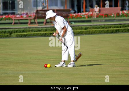 Une femme habillée de blancs appropriés utilise un maillet de croquet pour frapper des balles rouges et jaunes pendant la compétition dans les jardins gouvernementaux de Rotorua, en Nouvelle-Zélande, à l'été 2005. Banque D'Images