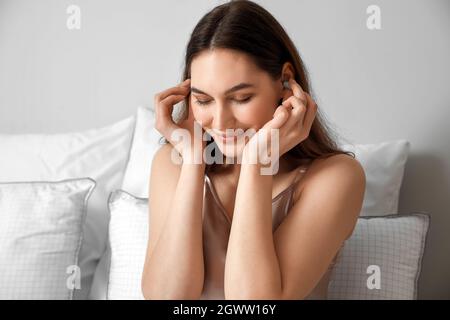 Belle jeune femme mettant des bouchons d'oreille avant de dormir dans la chambre Banque D'Images