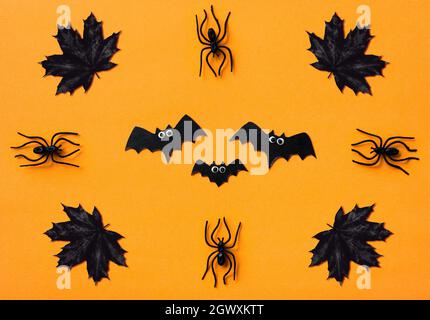 Décorations d'Halloween sur fond orange, plat. Vue de dessus des chauves-souris, des araignées noires et des feuilles d'érable. Motif sinistre avec des objets pour Hallowen celeb Banque D'Images