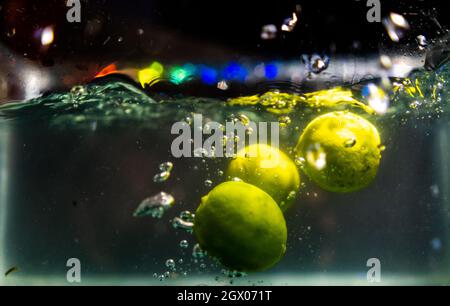 Trois limes fraîches tombent profondément dans l'eau avec des éclaboussures Banque D'Images