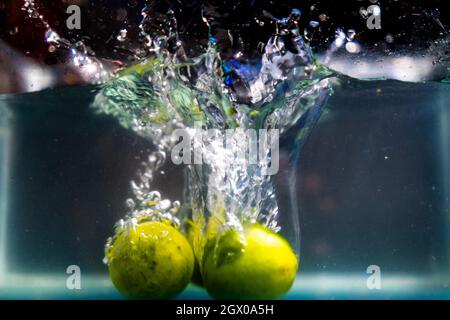 Trois limes fraîches tombent profondément dans l'eau avec des éclaboussures Banque D'Images