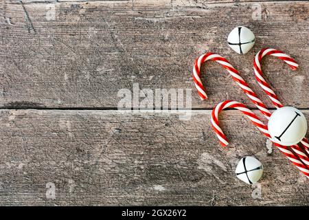 Arrière-plan de Noël avec des cannes rouges et blanches et des cloches blanches sur bois rustiques brun altéré. Vue de dessus. Banque D'Images