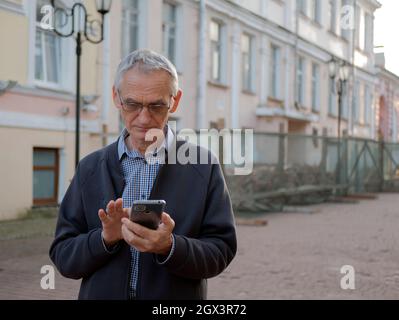 Une personne âgée dans les lunettes tient un téléphone portable dans ses mains. Un homme âgé envoie des SMS sur un smartphone. Le vieil homme utilise un téléphone portable Banque D'Images