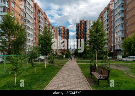 Les femmes marchent le long d'un trottoir carrelé en passant devant des immeubles en briques à plusieurs étages dans un quartier lors d'une journée d'été nuageuse. Banque D'Images