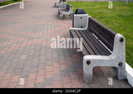 Des bancs en bois de rue avec une base en marbre sont debout depuis l'époque soviétique sur un trottoir pavé dans une rue de ville Banque D'Images