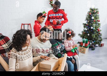 joyeux emballage familial afro-américain présente dans la salle de séjour avec arbre de noël flou Banque D'Images